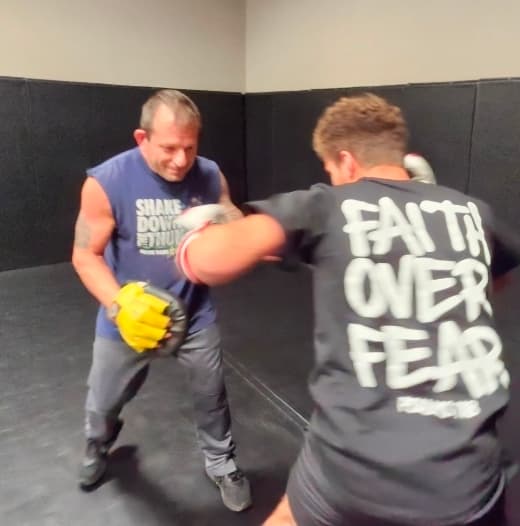 Coach Bud Wilson holding pads for a boxing student