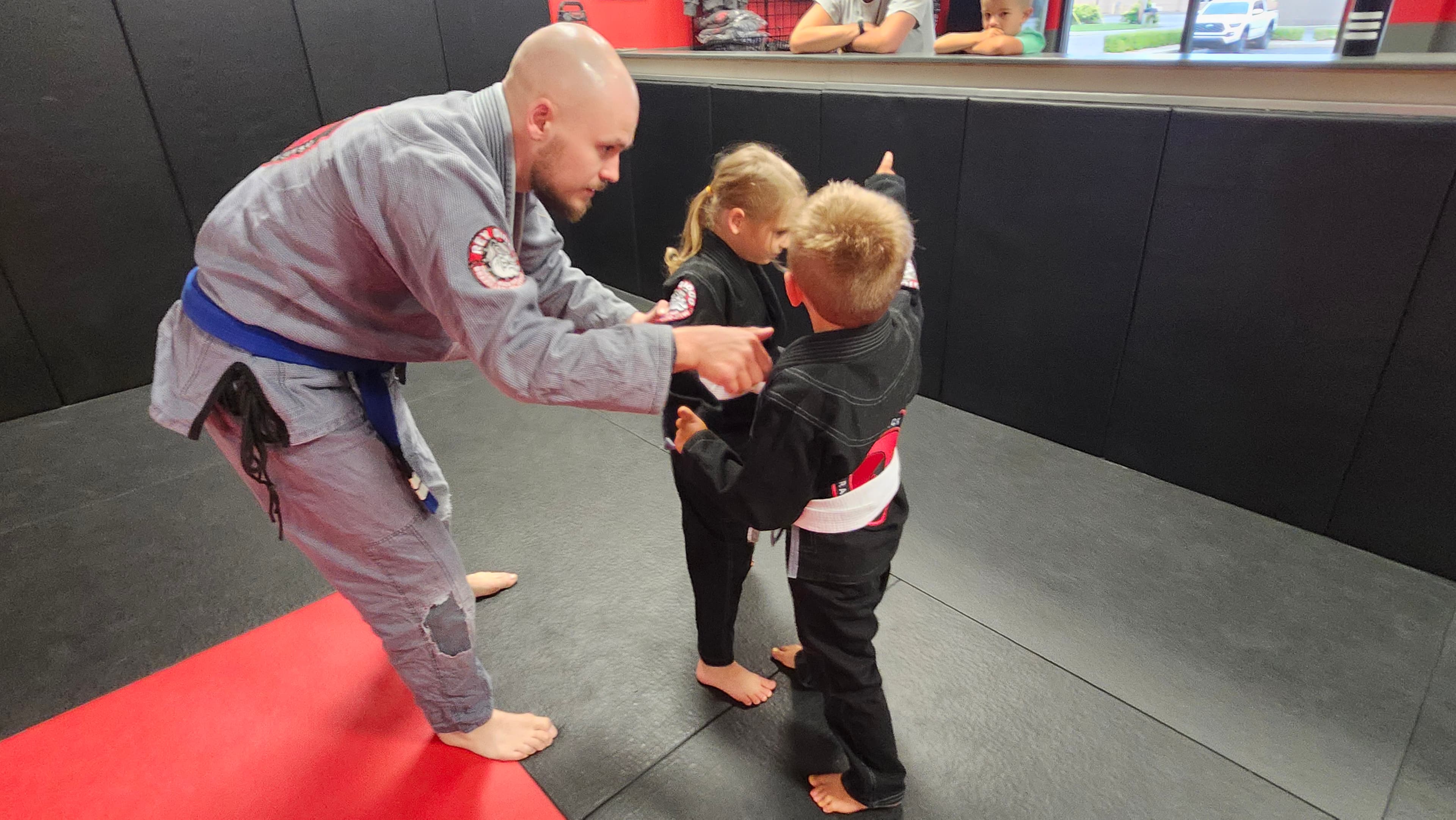 A coach guiding two young Barrick BJJ students through a technique