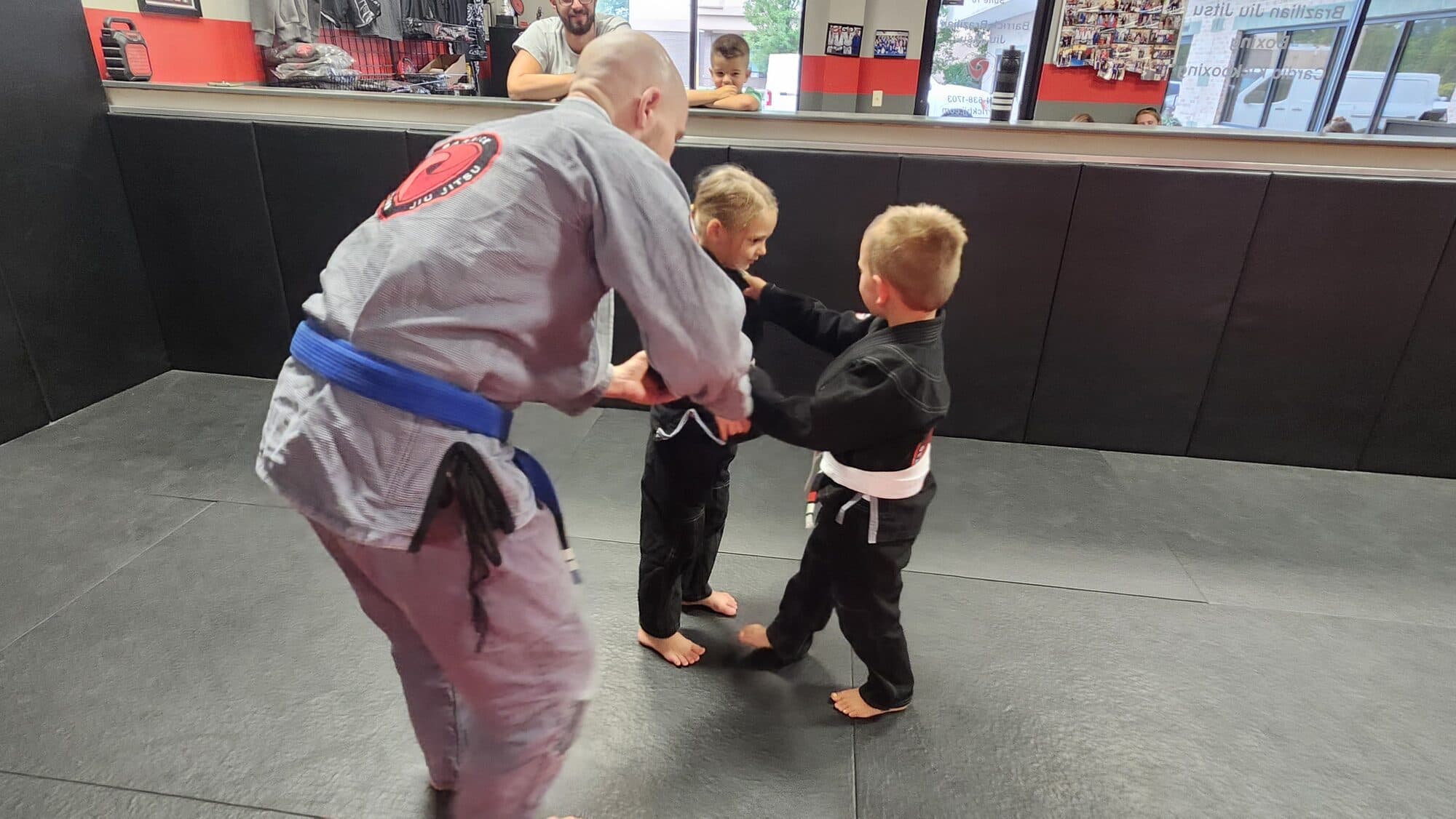 A Barrick BJJ coach teaching a self-defense technique to two young students in gis